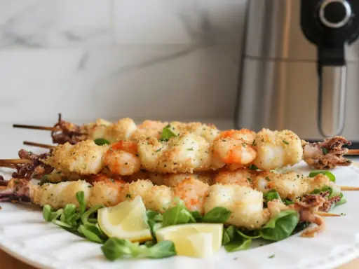 Spiedini di pesce croccanti, con gamberi e calamari impanati, serviti su un letto di insalata con spicchi di limone.