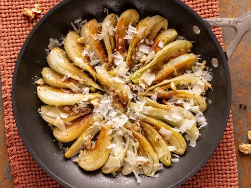 Finoçchi gratinati in padella, dorati e profumati, con scaglie di parmigiano e noci croccanti.