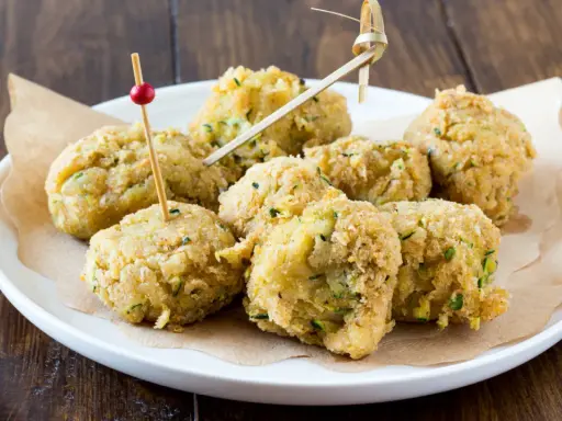 Polpette di ceci e zucchine dorate e croccanti, servite su un piatto bianco con stuzzicadenti decorativi.