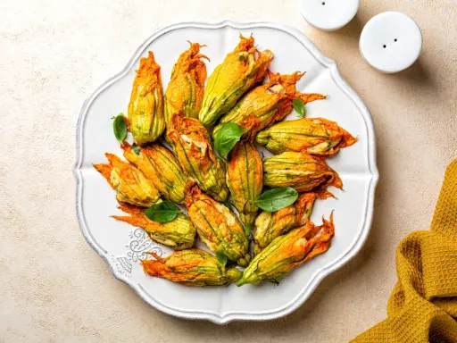 Fiori di zucca al forno ripieni, dorati e invitanti, disposti su un piatto bianco, con foglie di basilico fresco.
