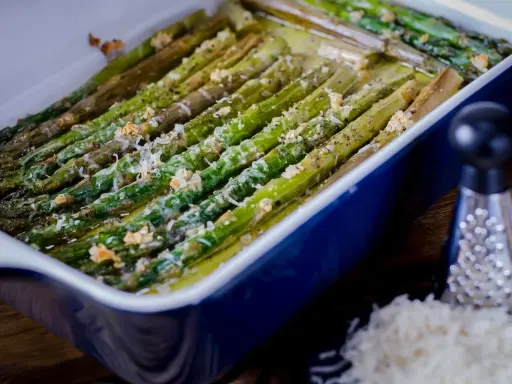 Asparagi al forno dorati e saporiti, conditi con formaggio grattugiato e pepe nero, pronti per essere gustati.