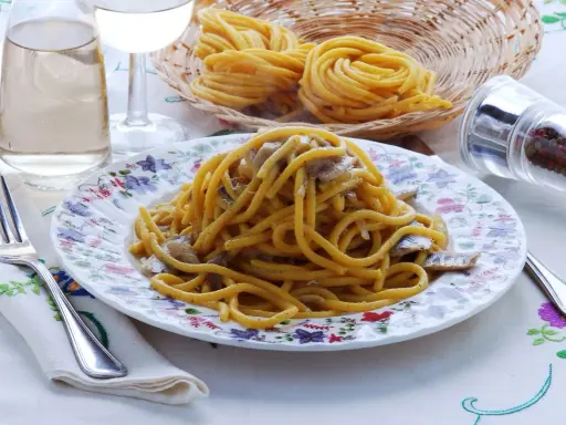 Un piatto di bigoli in salsa, con pasta fresca, acciughe e cipolla, pronto per essere gustato.