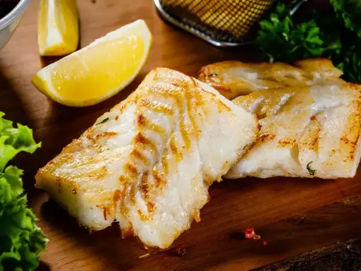 Spigola in padella al vino bianco, dorata e succulenta, servita con limone e insalata fresca su tagliere di legno.