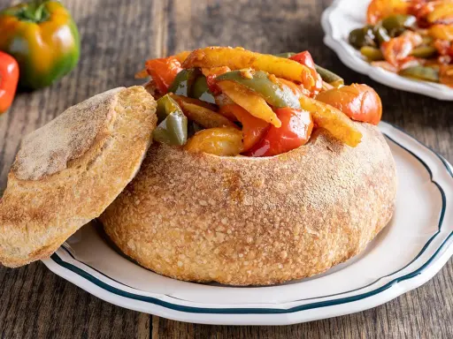 Pipi e patate in un pane scavato, un piatto rustico e colorato.