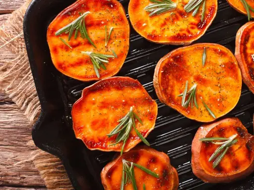 Fette di patate dolci grigliate in padella, condite con rosmarino e spezie, pronte per essere gustate.