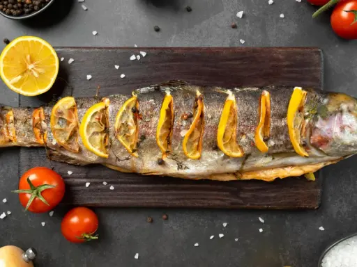 Un succulento pesce alla brace, guarnito con fette di limone e erbe aromatiche, pronto per essere gustato.