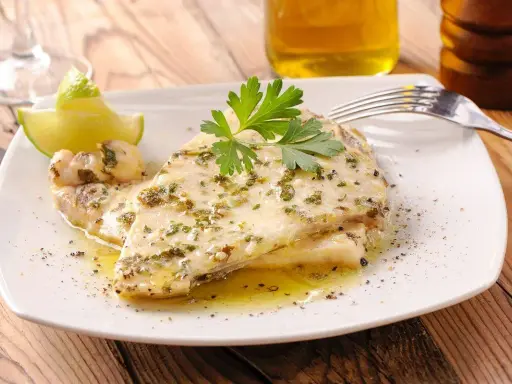 Delizioso pesce spada al forno, condito con erbe aromatiche e servito con spicchi di lime e prezzemolo fresco.