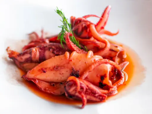 Totani in umido succulenti, cotti lentamente in un sugo saporito, guarniti con un rametto di finocchietto.