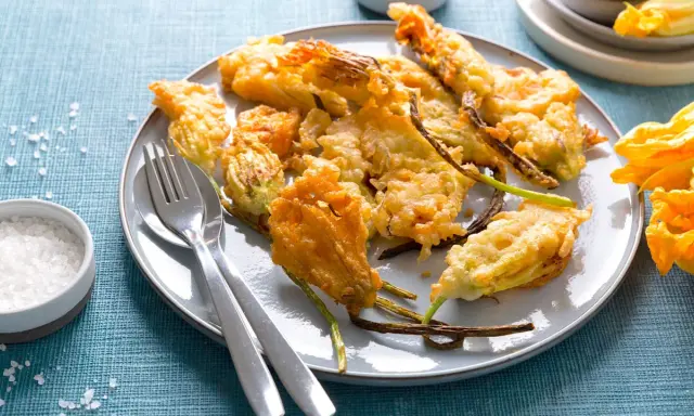 Piatto di fiori di zucca in pastella dorati e croccanti, serviti con sale grosso e posate.