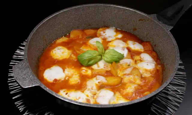 Patate alla pizzaiola in padella, con mozzarella filante e basilico fresco. Un piatto gustoso e invitante.