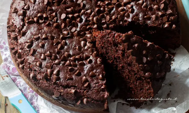 A rich, moist chocolate cake topped with chocolate chips, with a slice cut out to show its texture.
