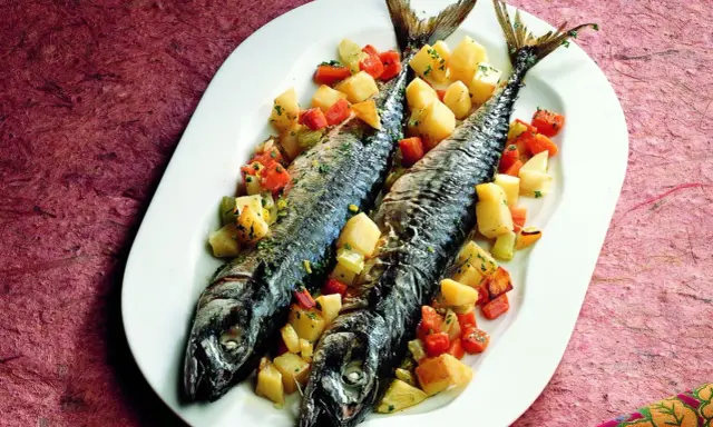 Due filetti di sgombro al forno, cotti alla perfezione, serviti con patate e carote a cubetti su un piatto bianco.