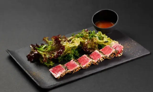 Tataki di tonno scottato, servito con insalata fresca e una ciotolina di salsa.