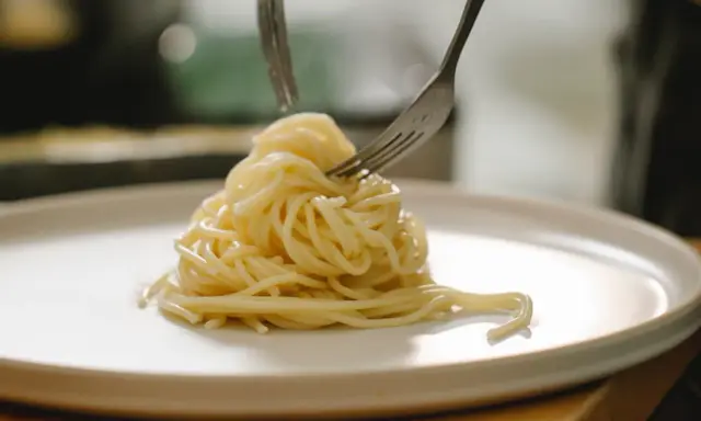 Spaghetti al limone serviti su un piatto bianco, con due forchette che raccolgono la pasta.