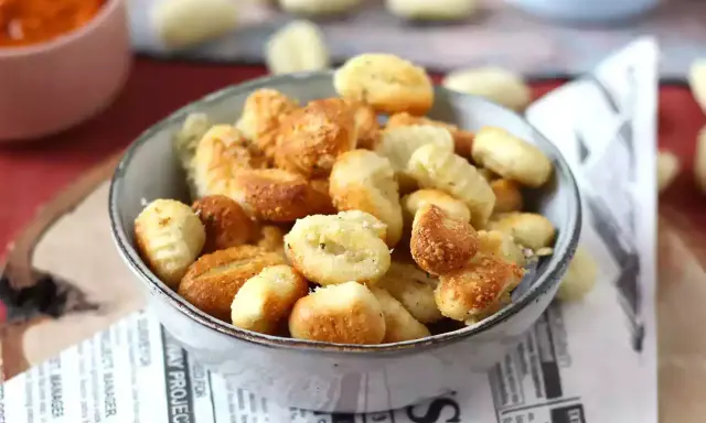 Gnocchi dorati e croccanti in friggitrice ad aria, serviti in una ciotola su carta di giornale.