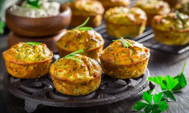 Tortini di zucchine dorati e fragranti, guarniti con rosmarino, su un piatto di ghisa. Sullo sfondo, una ciotola di formaggio fresco.