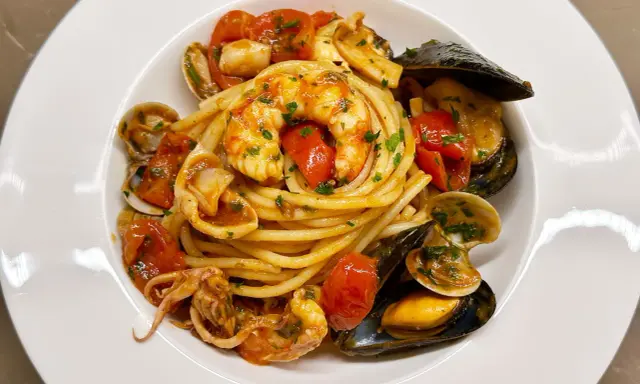 Un invitante piatto di spaghetti allo scoglio, con gamberi, cozze, vongole e calamari, condito con pomodorini e prezzemolo.