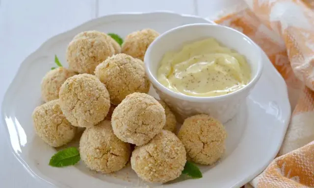 Polpette di ceci al forno dorate e croccanti, servite su un piatto bianco con una ciotolina di salsa cremosa e foglie di menta.