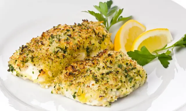 Delizioso merluzzo al forno con crosta croccante di erbe e pangrattato, guarnito con spicchi di limone e prezzemolo fresco.