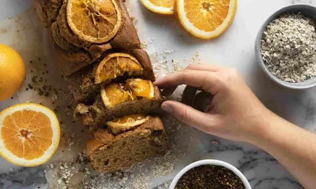 Un profumato plumcake all'arancia, uno dei tanti dolci senza glutine, pronto per essere gustato. Accanto, arance fresche e avena.