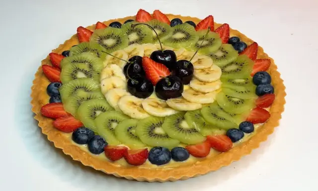 A fruit tart with kiwi, banana, strawberries, blueberries, and cherries on a custard filling.