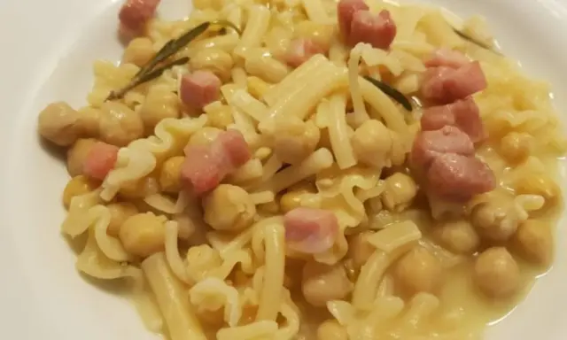 Un piatto di pasta e ceci in scatola, arricchito da cubetti di pancetta e un rametto di rosmarino.