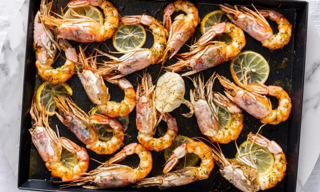 Gamberoni al forno dorati e succulenti, conditi con erbe aromatiche e spicchi di limone, pronti per essere gustati.