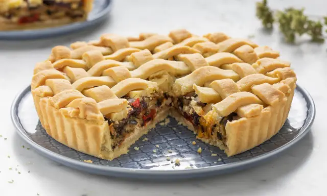 Una crostata morbida salata con verdure miste, peperoni e melanzane, ricoperta da una griglia di pasta dorata.