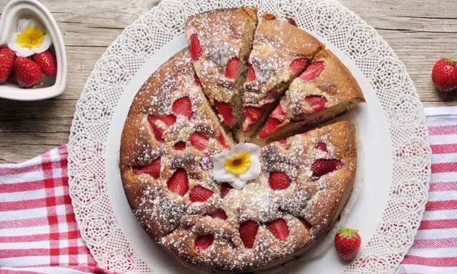 Torta di fragole e yogurt, soffice e profumata, cosparsa di zucchero a velo e decorata con un fiore. Perfetta per una colazione o merenda.
