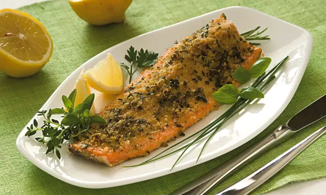 Deliziosa trota salmonata al forno, croccante e profumata, servita con limone e erbe aromatiche fresche.