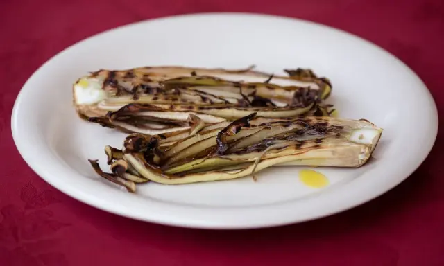 Radicchio in padella, grigliato e caramellato, servito su un piatto bianco con un filo d'olio.