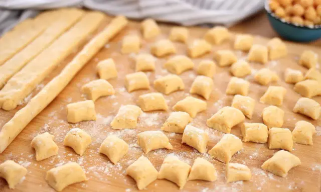 Piccoli gnocchi di ceci sparsi su un tagliere di legno, pronti per essere cotti.
