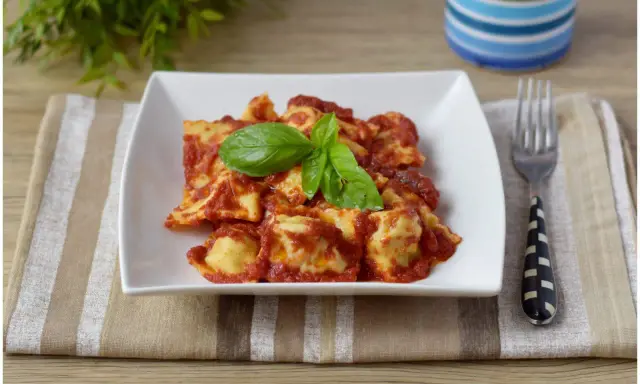 Un piatto di ravioli di carne conditi con sugo rosso e basilico fresco, pronti per essere gustati.
