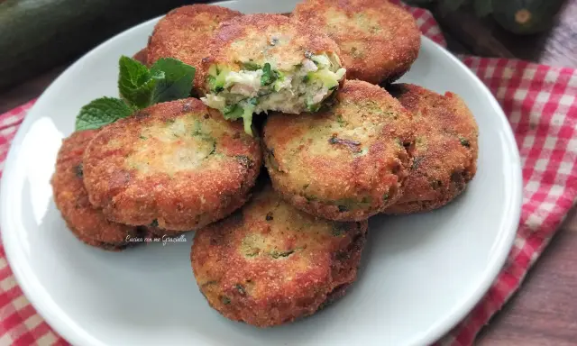 Piatto di polpette di zucchine e ricotta dorate e croccanti, guarnite con menta fresca.