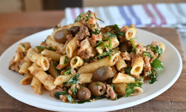 Piatto di pasta al tonno con olive verdi e prezzemolo fresco, servita su un piatto bianco.