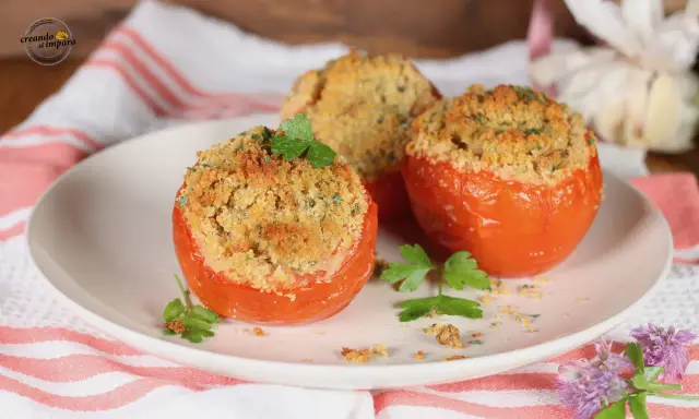 Tre pomodori gratinati al forno, ripieni e dorati, guarniti con prezzemolo fresco su un piatto bianco.