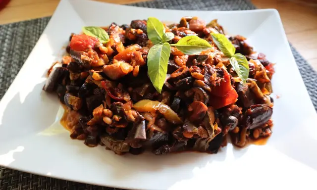 Un piatto di saporita caponata di melanzane, guarnita con foglie di basilico fresco.