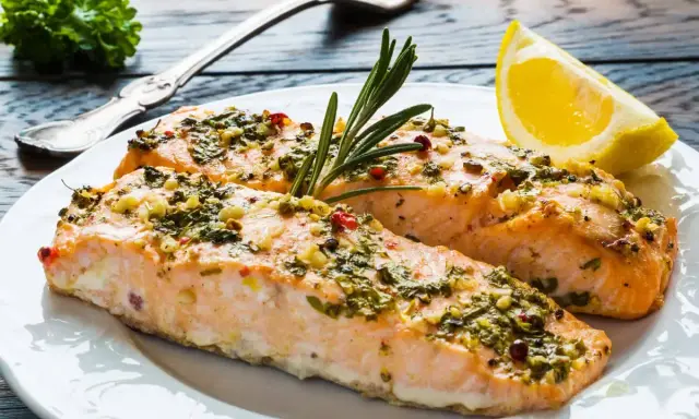 Delizioso salmone al forno con erbe aromatiche, aglio e peperoncino, guarnito con rosmarino e una fetta di limone.
