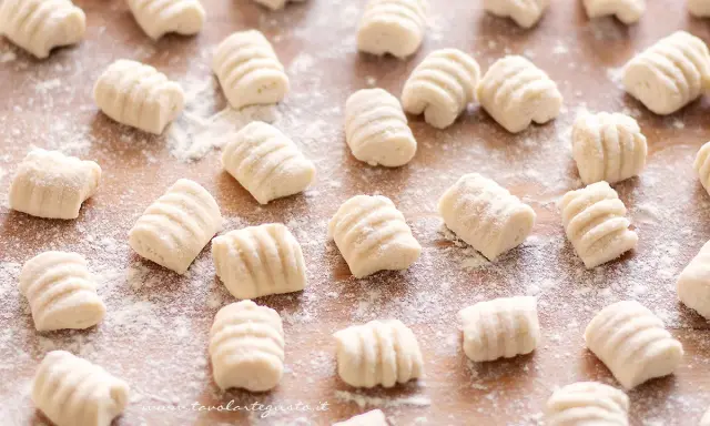 Gnocchi di ricotta freschi, pronti per essere cucinati, spolverati di farina su un tagliere di legno.