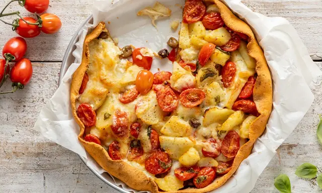 Torta salata con patate, pomodorini e formaggio filante, un piatto rustico e gustoso, pronto per essere gustato.