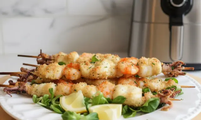 Spiedini di pesce croccanti, con gamberi e calamari impanati, serviti su un letto di insalata con spicchi di limone.