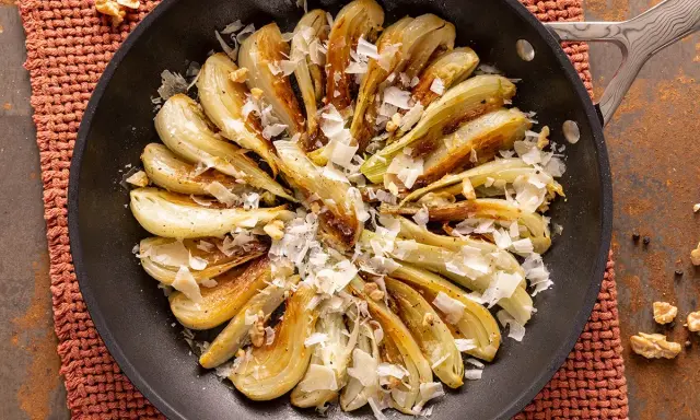 Finoçchi gratinati in padella, dorati e profumati, con scaglie di parmigiano e noci croccanti.