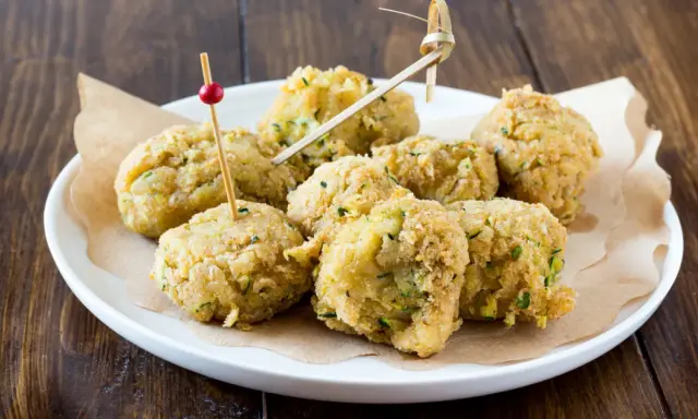 Polpette di ceci e zucchine dorate e croccanti, servite su un piatto bianco con stuzzicadenti decorativi.