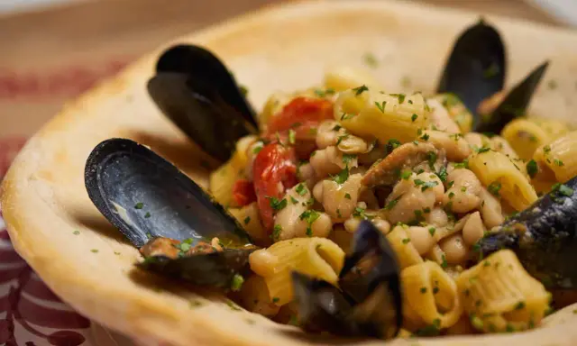 Un piatto invitante di pasta fagioli e cozze, con pomodorini e prezzemolo fresco, servito in una ciotola di pane croccante.