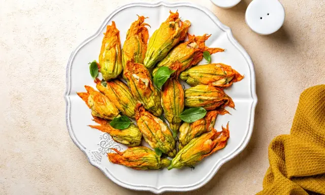 Fiori di zucca al forno ripieni, dorati e invitanti, disposti su un piatto bianco, con foglie di basilico fresco.