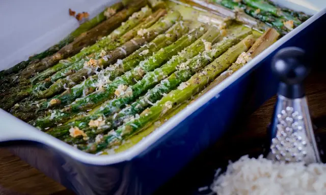 Asparagi al forno dorati e saporiti, conditi con formaggio grattugiato e pepe nero, pronti per essere gustati.