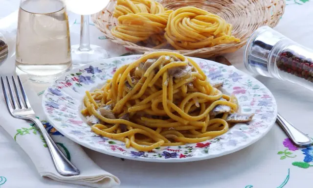 Un piatto di bigoli in salsa, con pasta fresca, acciughe e cipolla, pronto per essere gustato.