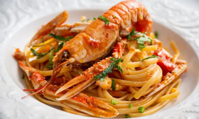 Un piatto invitante di linguine agli scampi, con pasta fresca e scampi succulenti conditi con un sugo saporito e prezzemolo tritato.