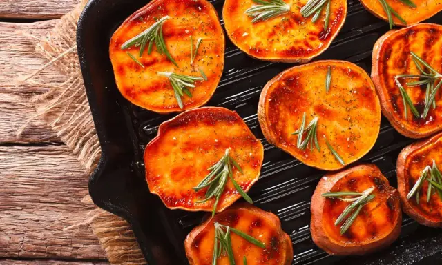 Fette di patate dolci grigliate in padella, condite con rosmarino e spezie, pronte per essere gustate.