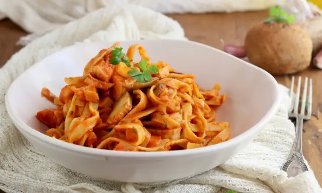 Un piatto invitante di tagliatelle ai funghi, condite con una ricca salsa al pomodoro e guarnite con prezzemolo fresco.